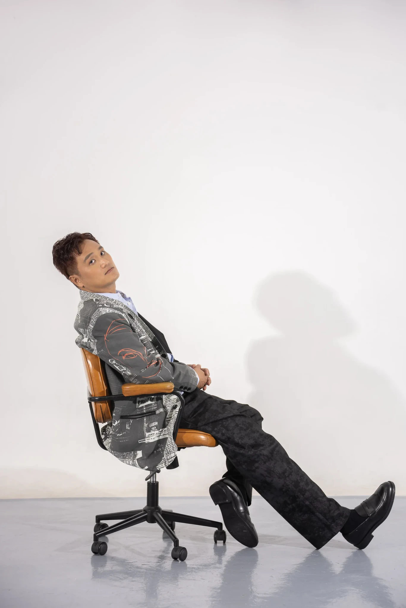 Peter Huang of MICappella seated in a brown leather chair in a grey newsprint-patterned blazer