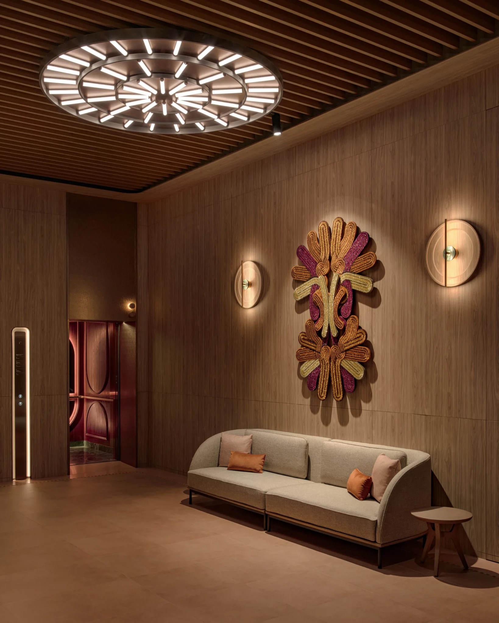 The APT. lobby at Stamford Place with a wood-slatted ceiling, circular light fixture, grey sofa and textile wall artwork