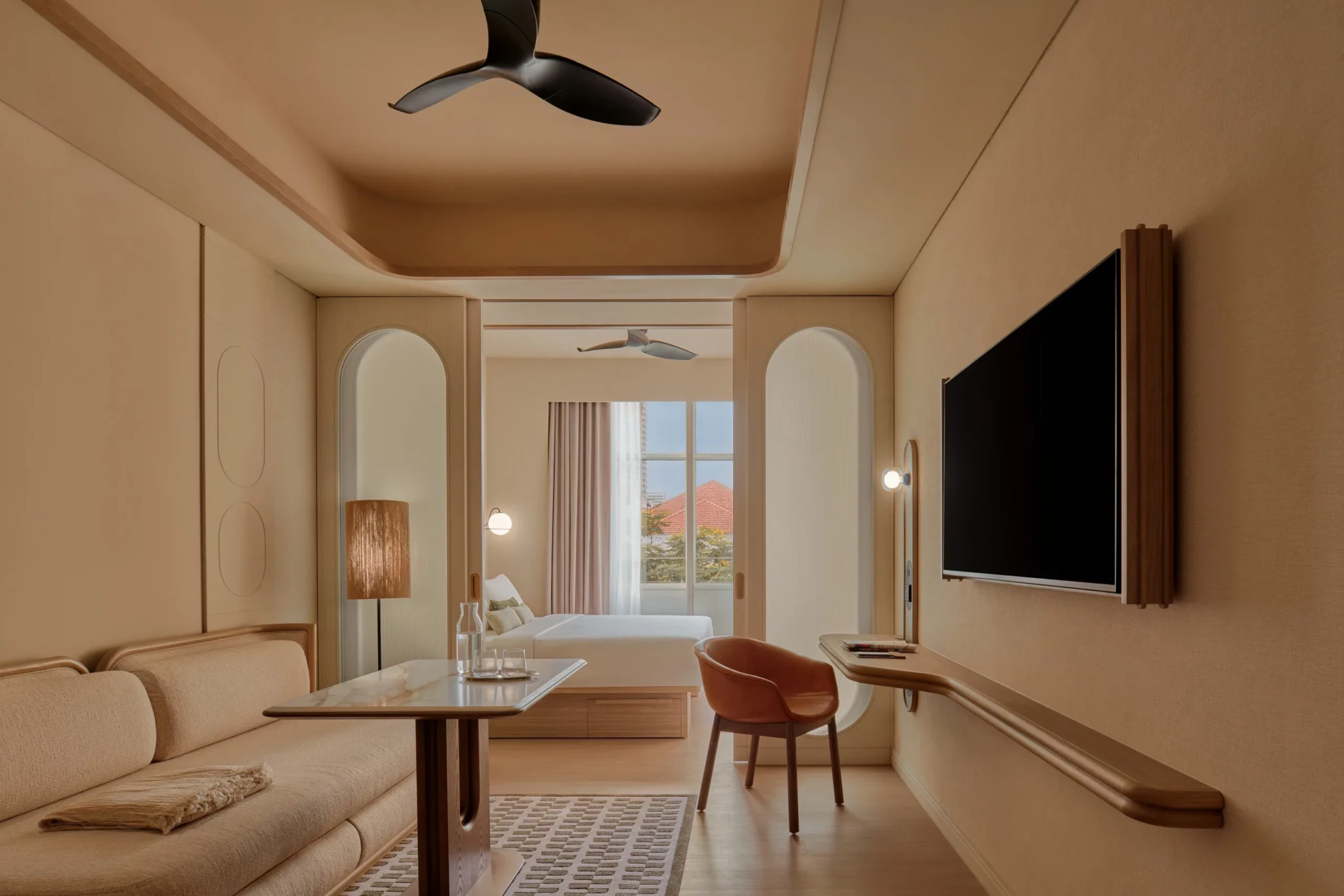 A guest room at APT. at Stamford Place, Singapore, with a warm neutral palette, arched wall recesses, a wall-mounted television, a leather armchair and a view o