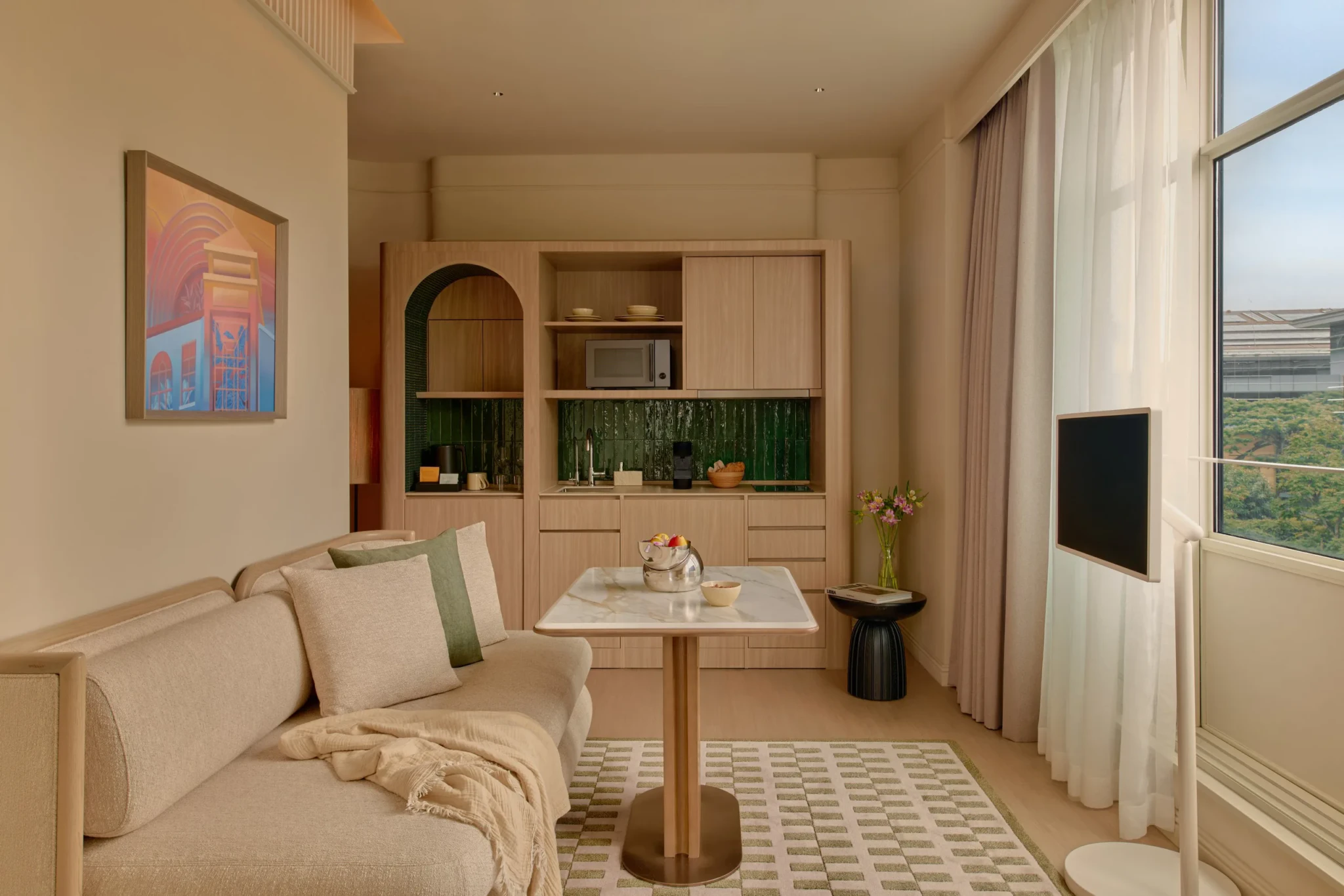 The Civic Suite living room with a beige sofa, marble-top dining table and green-tiled kitchenette