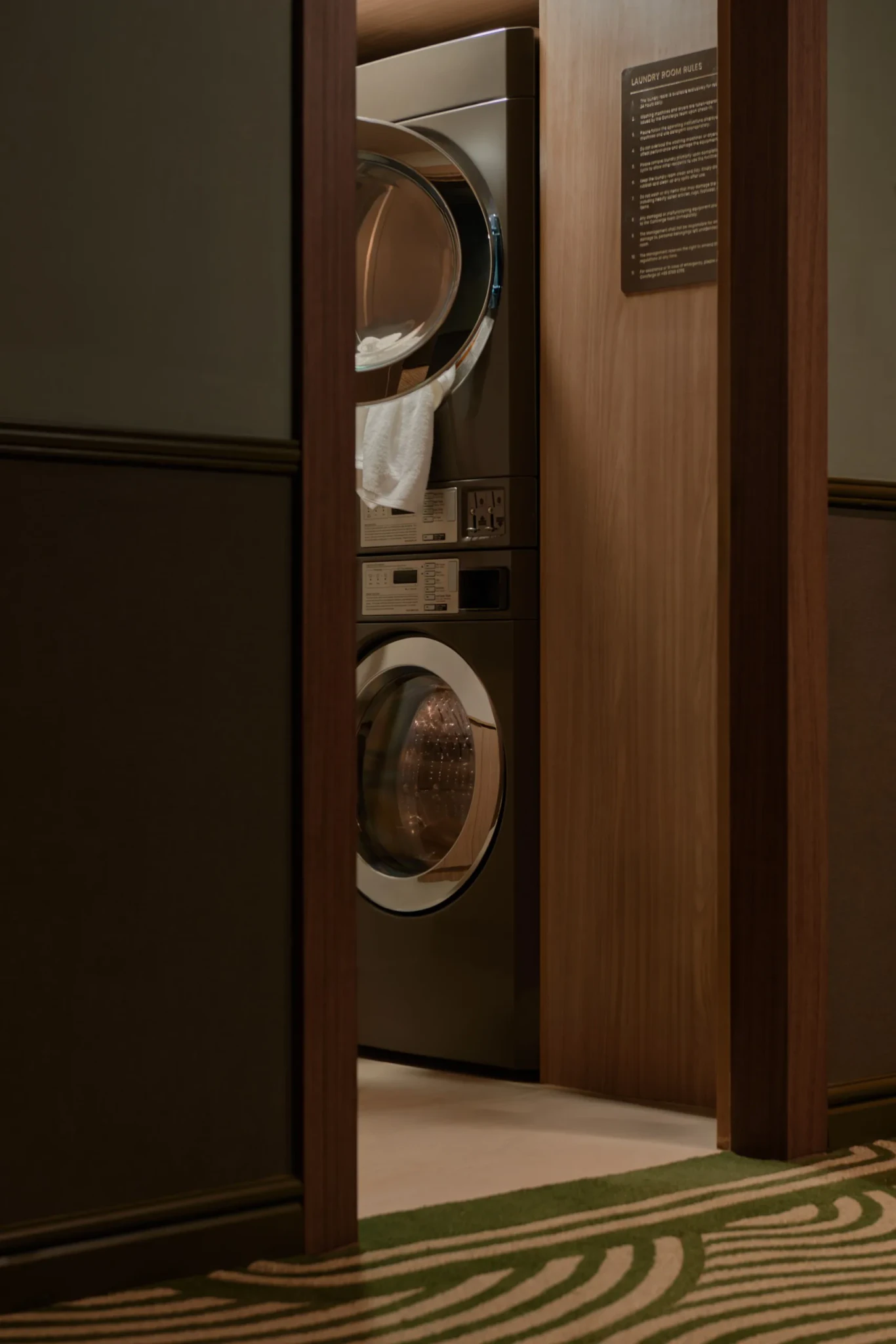A stacked washer and dryer behind a wooden door with a Laundry Room Rules placard